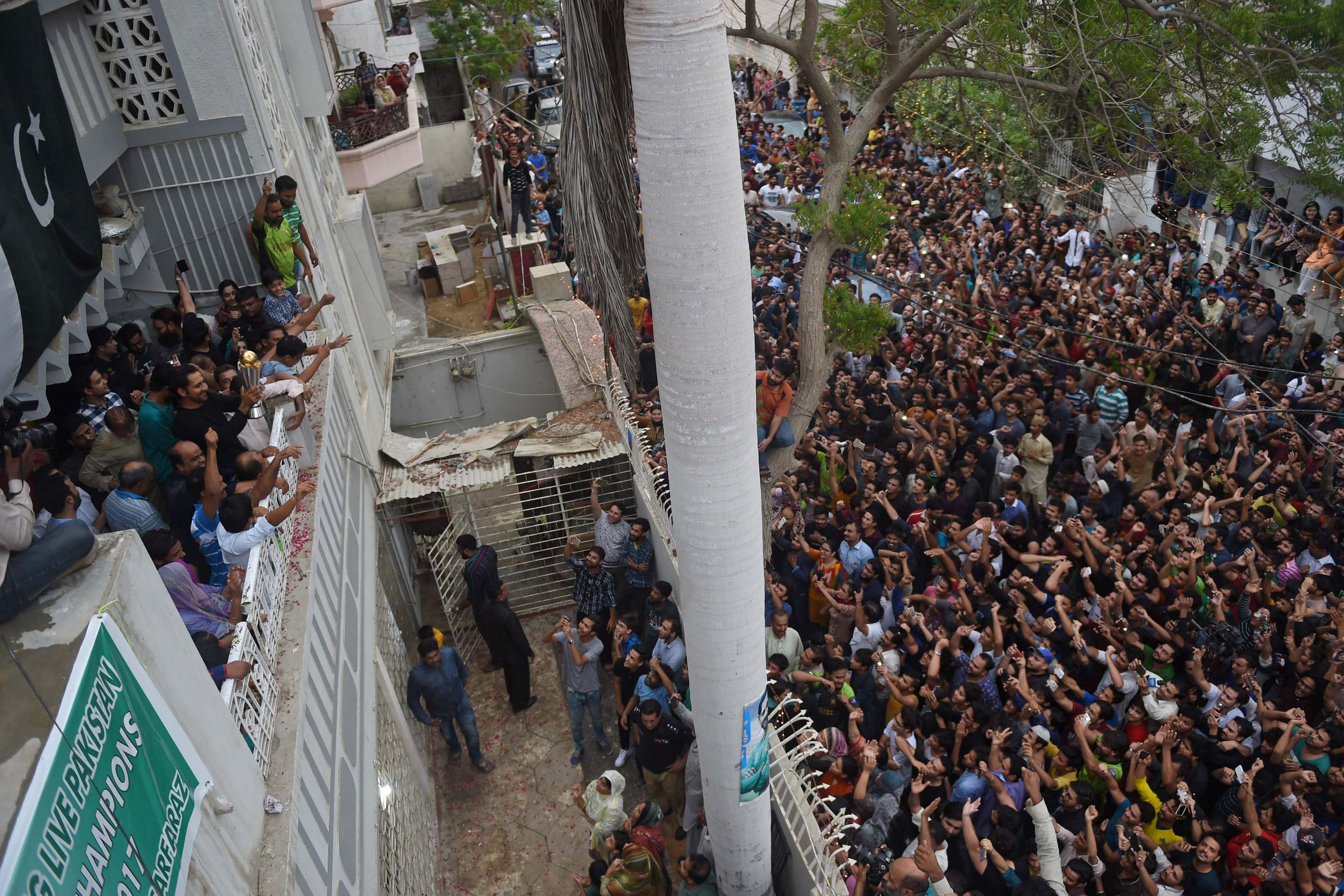 Sarfaraz Ahmed (L, in black shirt) holds the trophy as he acknowledges fans at his home.