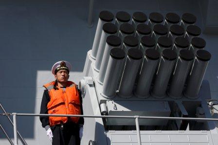A Chinese serviceman stands beside a multibarrel rocket launcher on the deck of a naval vessel.