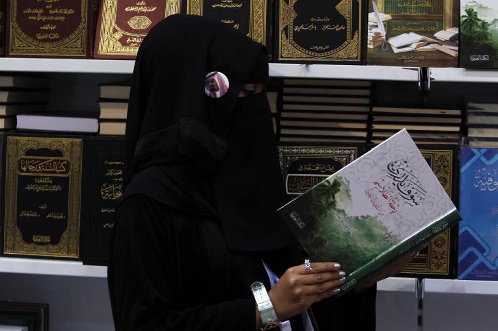 A veiled woman wearing a badge with a portrait of Saudi King Abdullah browses a book at the Riyadh International Book Fair, March 6, 2012. REUTERS