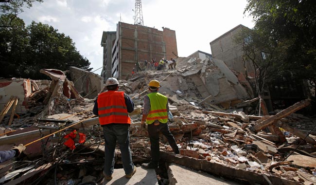 Rescue workers look at fellow workers searching for people under the rubble of a collapsed building