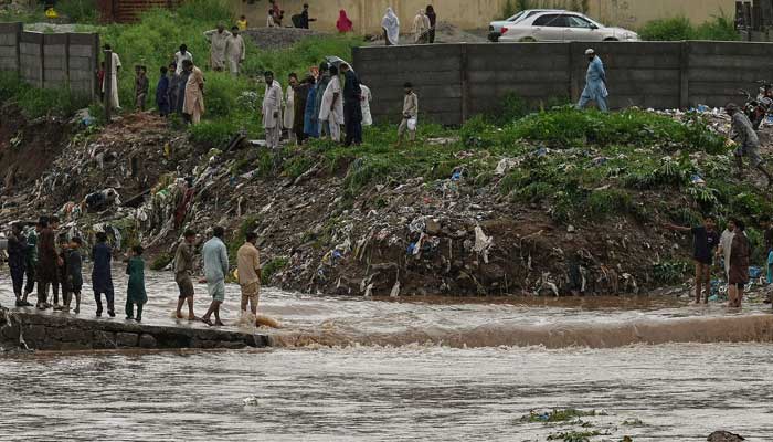 Residents cross a stream of water on a road that was flooded after heavy monsoon rains in Islamabad on July 28, 2021.-AFP