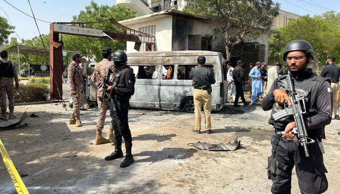 Law-enforcers stand guard around the vehicle bombed at Karachi Universitys entrance on April 26, 2022. Photo: Twitter