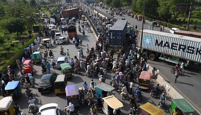 Commuters try to make their along a road partially blocked with containers by local authorities to hinder mobility ahead of the sit-in planned in Islamabad by PTI in Lahore on May 24, 2022. -AFP