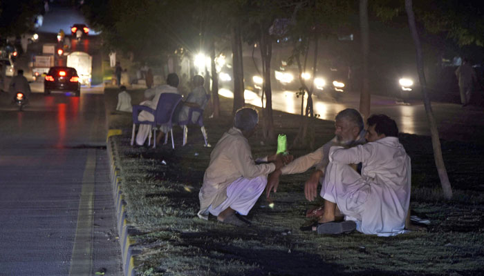 People sitting on a green belt alongside a road in Sector G7 of Islamabad during the span of loadshedding in the federal capital on June 14, 2022. Photo: Online