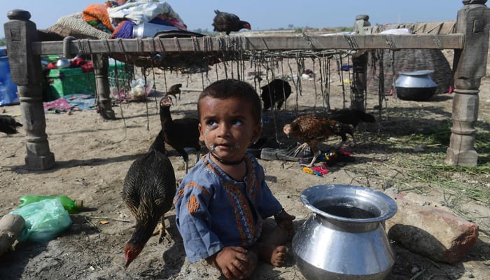 A child sits on a dry ground near by his family after fleeing from flood-hit home in Shikarpur of Sindh province on August 30, 2022.-AFP