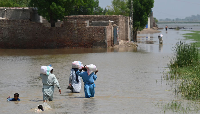 Flood-affected people wade through a flooded area with relief food bags as they return their homes on the outskirts of Jacobabad, Sindh province, on September 6, 2022. —AFP/ Aamir QURESHI