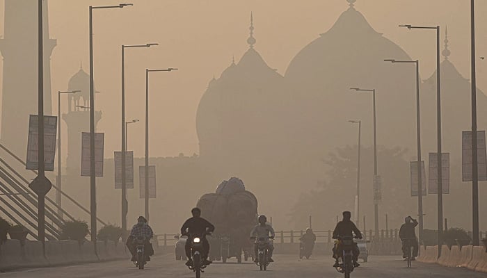Commuters ride along a road amid smoggy conditions in Lahore on November 16, 2021. —AFP