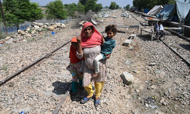 Fahmidah, a pregnant flood-affected woman carries her child as she walks near her tent at a makeshift camp along a railway track in Fazilpur, Rajanpur district of Punjab province on September 3, 2022. —AFP