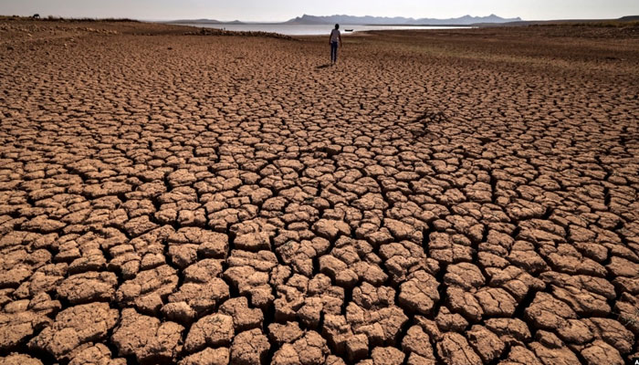 A woman walks over cracked earth at al-Massira dam in Ouled Essi Masseoud village, some 140 kilometers south from Moroccos economic capital, Casablanca, on August 8, 2022. — AFP
