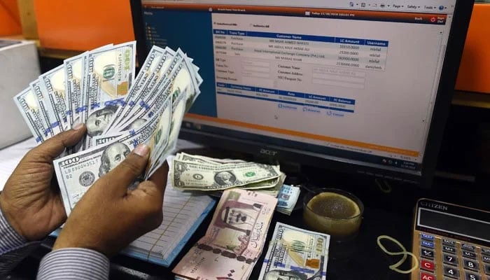A dealer counts US dollars at a currency exchange shop in Karachi. — AFP/File