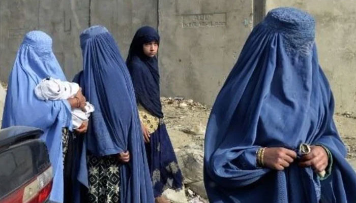 This photograph taken on Oct 2, 2019, an Afghan woman (L) holds an infant next to other burqa-clad women on a street in Kabul. AFP