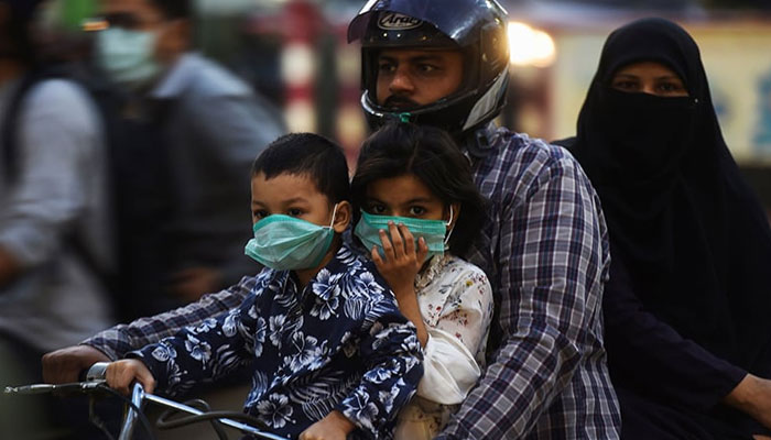 Children riding on a bike with their family wear facemasks as a preventive measure against the coronavirus in Karachi on October 29. — AFP