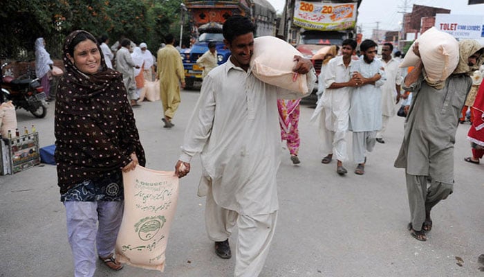 A representational image of people carrying flour bags after purchase from a sale point. — AFP/File