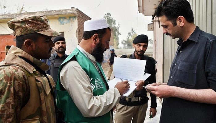 An official from the Pakistan Bureau of Statistics collects information from a resident during a census as security personnel guard them in Peshawar.— AFP