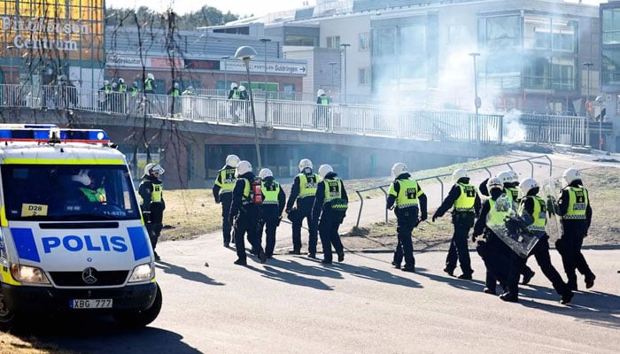 Riot police pass a barricade to enter a shopping center during rioting in Norrkoping, Sweden on 17 April 2022. — AFP