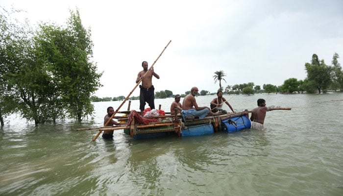 Residents use a makeshift raft to make their way through flood waters in Rajanpur. — AFP/File