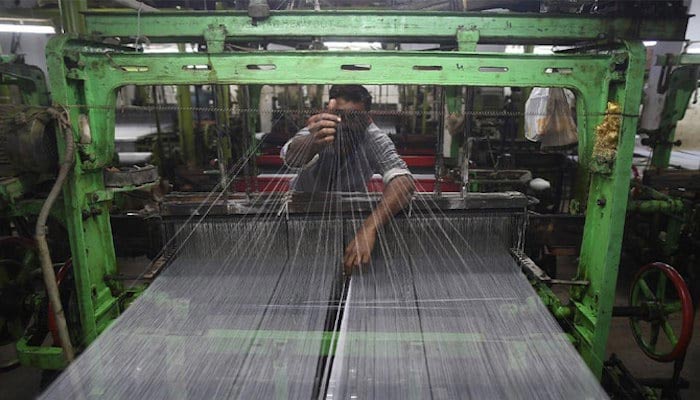 A Pakistan textile labourer fixes broken threads at a power loom in Karachi, the financial capital and the largest industrial city of Pakistan. — AFP/File