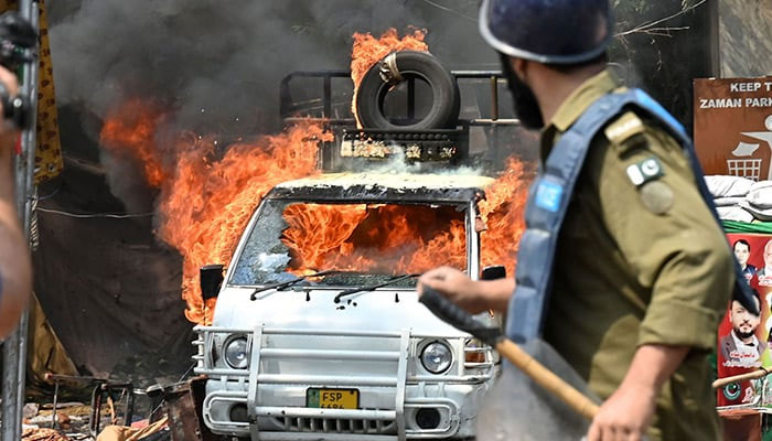 A policeman stands near a burning vehicle during clashes between supporters of former prime minister Imran Khan and riot police near Khans house to prevent officers from arresting him, in Lahore on March 15, 2023. — AFP