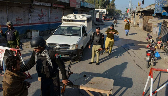 Police stand guard along a road they blocked after militants seized a police station in Bannu on December 19, 2022. — AFP