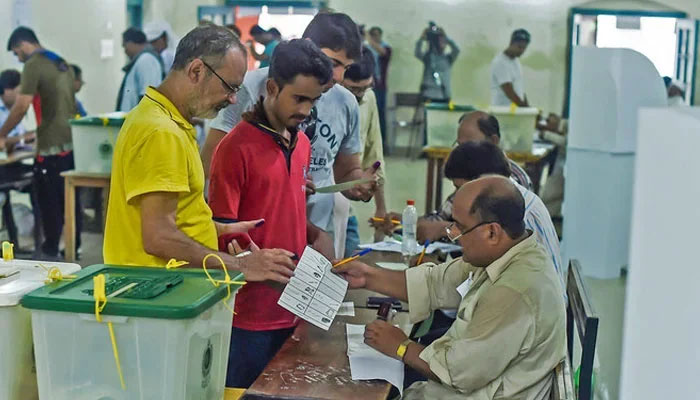 Men line up as election officials check their ballot papers during voting in general election at a polling station in Lahore on July 25, 2018. — AFP