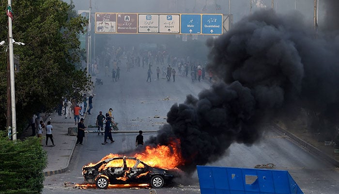 A car is seen burning along a road as Pakistan Tehreek-e-Insaf (PTI) party activists and supporters of former Pakistan´s Prime Minister Imran block a road during a protest against the arrest of their leader in Karachi on May 9, 2023. — AFP
