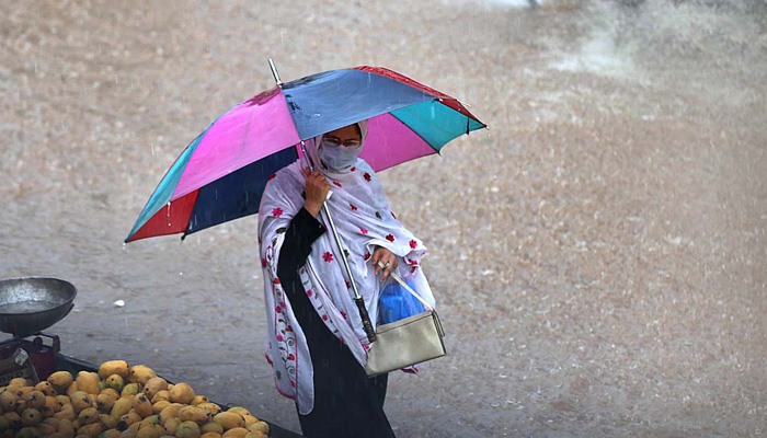 A woman walks through rain water under the cover of an umbrella during rain in Islamabad on July 27, 2023. — APP
