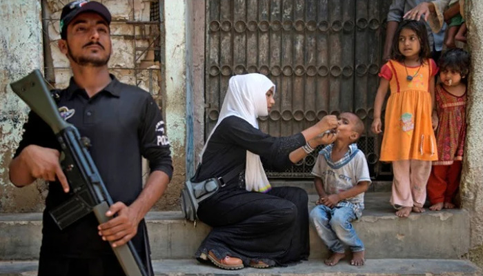 A cop stands guard as a health worker administers the polio vaccine to a child during a vaccination campaign in Karachi. — AFP