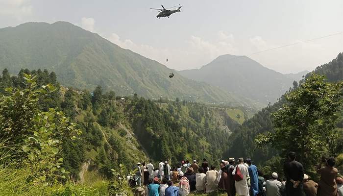 People watch as an army soldier slings down from a helicopter during a rescue mission to recover students stuck in a chairlift in a village of mountainous Khyber Pakhtunkhwa on August 22, 2023. — AFP