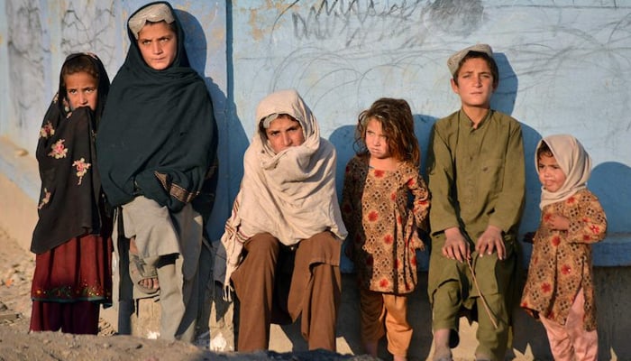Children bask in the sun next to a wall along a street in Nad Ali district, Helmand province on November 10, 2021. — AFP