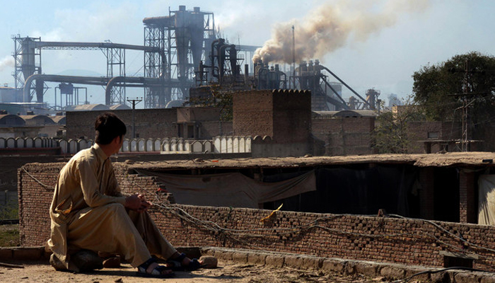 This file photo shows a Pakistani worker watching smoke rising from factories on the outskirts of the northwestern city of Peshawar. — AFP/File