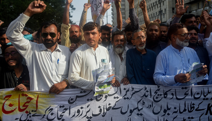 Traders shout slogans as they hold a banner reading we demand the government to withdraw the additional electricity bills during a protest against the surge in electricity prices along a street in Karachi on August 30, 2023. — AFP