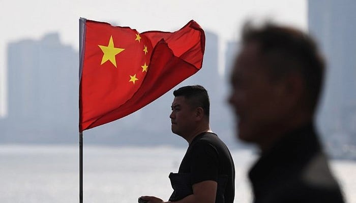Two Chinese men stand near a Chinese flag as they look out towards North Korea while visiting the Broken Bridge in the Chinese border city of Dandong in Chinas northeast Liaoning. — AFP/File