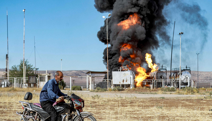 A man prepares to ride a motorcycle close to a fire raging at the Zarba oil facility in al-Qahtaniyah in northeastern Syria close to the Turkish border on October 5, 2023. — AFP