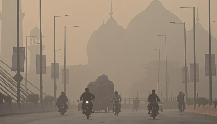 Commuters ride along a road amid smoggy conditions in Lahore on November 16, 2021. — AFP