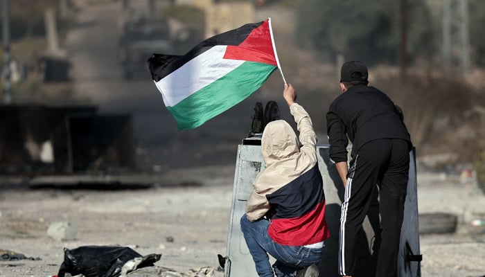 Palestinian boys wave their national flag as demonstrators clash with Israeli soldiers during a protest in Ramallah in the occupied West Bank on October 18, 2023. — AFP