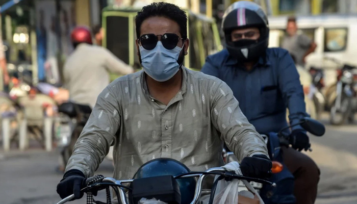 Two people can be seen wearing facemasks while they ride motorcycles on a street in Lahore. — AFP/File