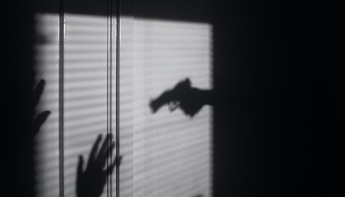A representational image of a shadow showing a gun pointed towards hands. — Unsplash/File