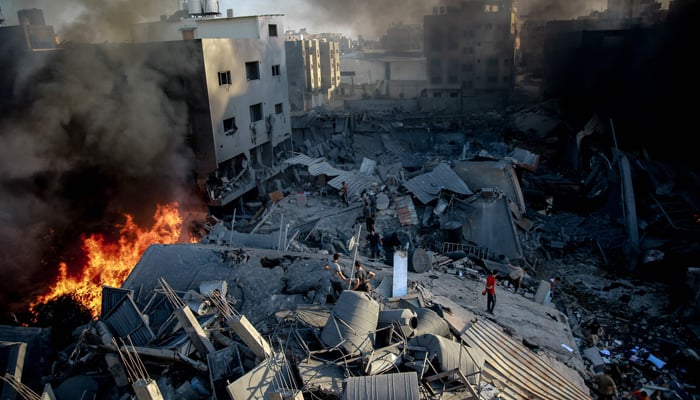 Smoke and fire rise from a levelled building as people gather amid the destruction in the aftermath of an Israeli strike on Gaza City on October 26, 2023. — AFP
