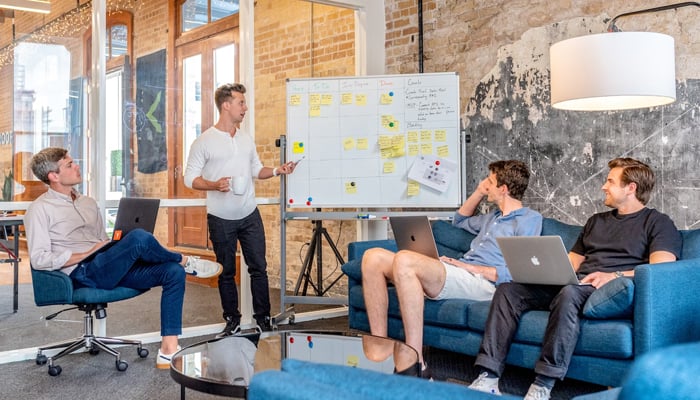 A representational image of people interacting in a professional environment with one of them explaining a board. — Unsplash