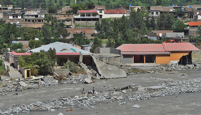 A representational image shows local residents standing near houses damaged along the banks of a river in Pakistan. — AFP/File