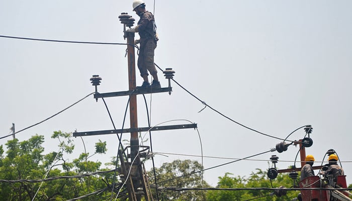 Men work on electric pylons along the roadside in Karachi. — AFP/File