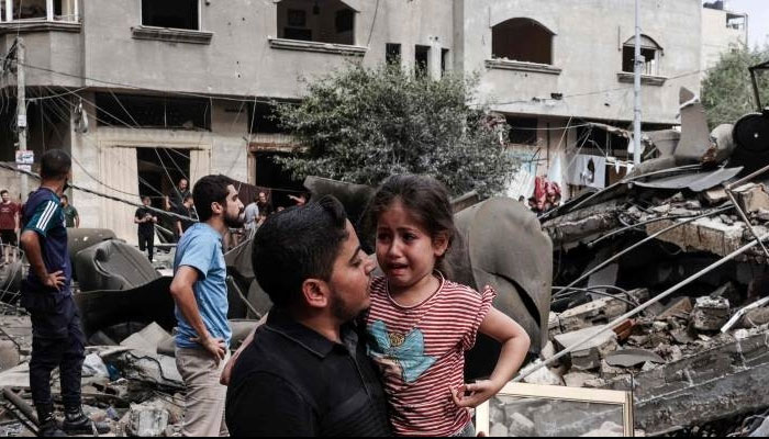 A man carries a crying child as he walks in front of a building destroyed in an Israeli air strike in Gaza City Saturday. — AFP