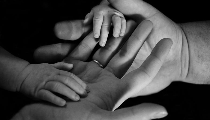 A representational image shows the hands of two adults and an infant. — Unsplash/File