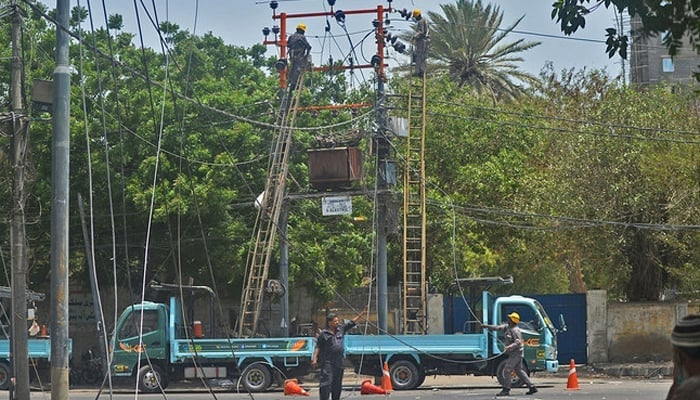 Men work on electric pylons along the roadside in Karachi. — AFP/File