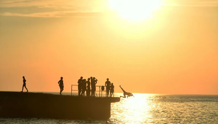 The image shows heat-weary people one of whom jumps into water. — AFP FILE