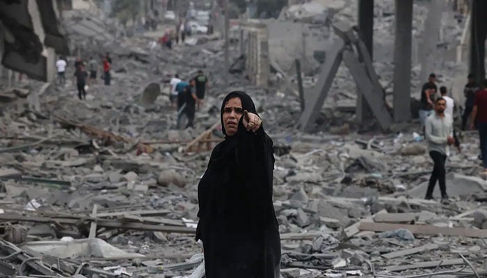 A woman points to the camera while a wholly destructed area can be seen in the background as a result of continuous bombing by Israeli forces. — AFP/File