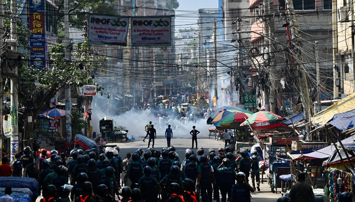 Bangladesh police (foreground) stand guard along a road during clashes with garment workers (top) protesting to demand an increase in their salaries, in Dhaka on November 2, 2023. — AFP