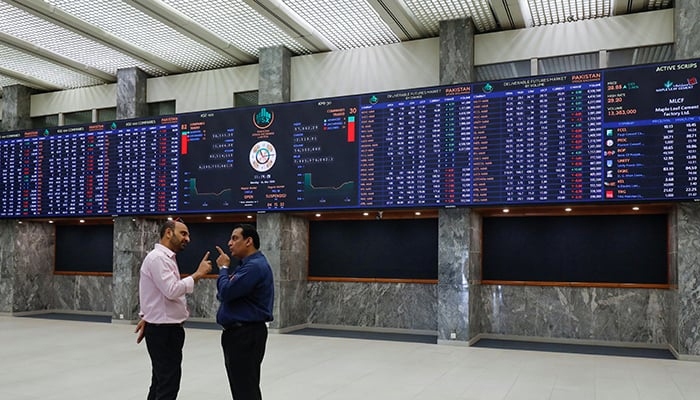 Two investors can be seen discussing in front of the digital stock board at the Pakistan Stock Exchange. — AFP/File