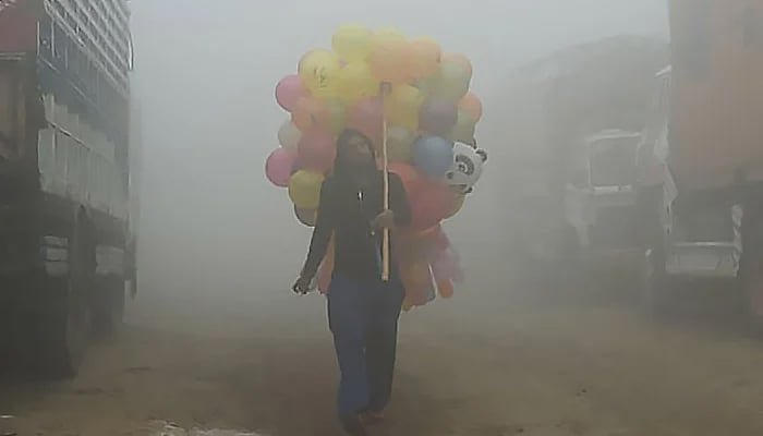A vendor carries balloons down a Lahore street amid heavy smog. — AFP/File