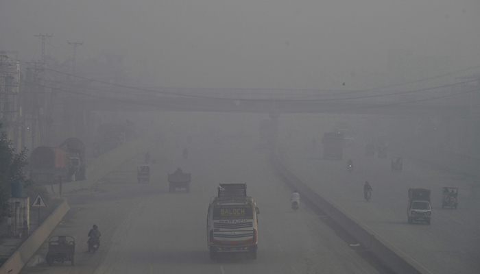 Commuters make their way along a road amid smoggy conditions in Lahore on November 14, 2023. — AFP